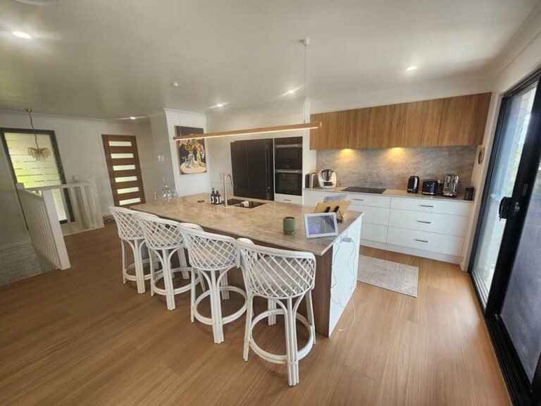 Open-concept kitchen with a large island, white lattice stools, and wood accents under a suspended pendant light.
