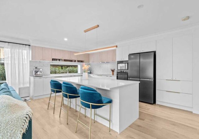 Bright, modern kitchen with a white island, teal bar stools, and a stainless steel refrigerator.