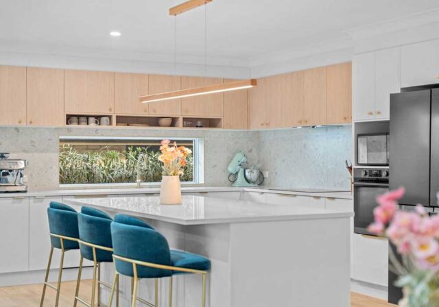 Bright modern kitchen with a large white island, teal bar stools, and light wood cabinets.