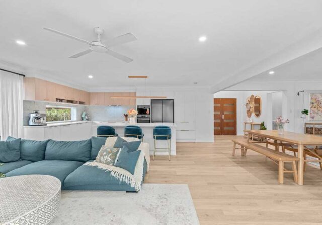 Open-plan living area with a blue sectional sofa, white cabinetry, and a kitchen island with three blue barstools.