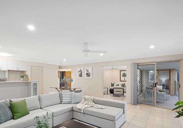 Open-concept living room with a light gray L-shaped sofa, green cushions, and a throw blanket, plus sliding doors to a patio on the right.